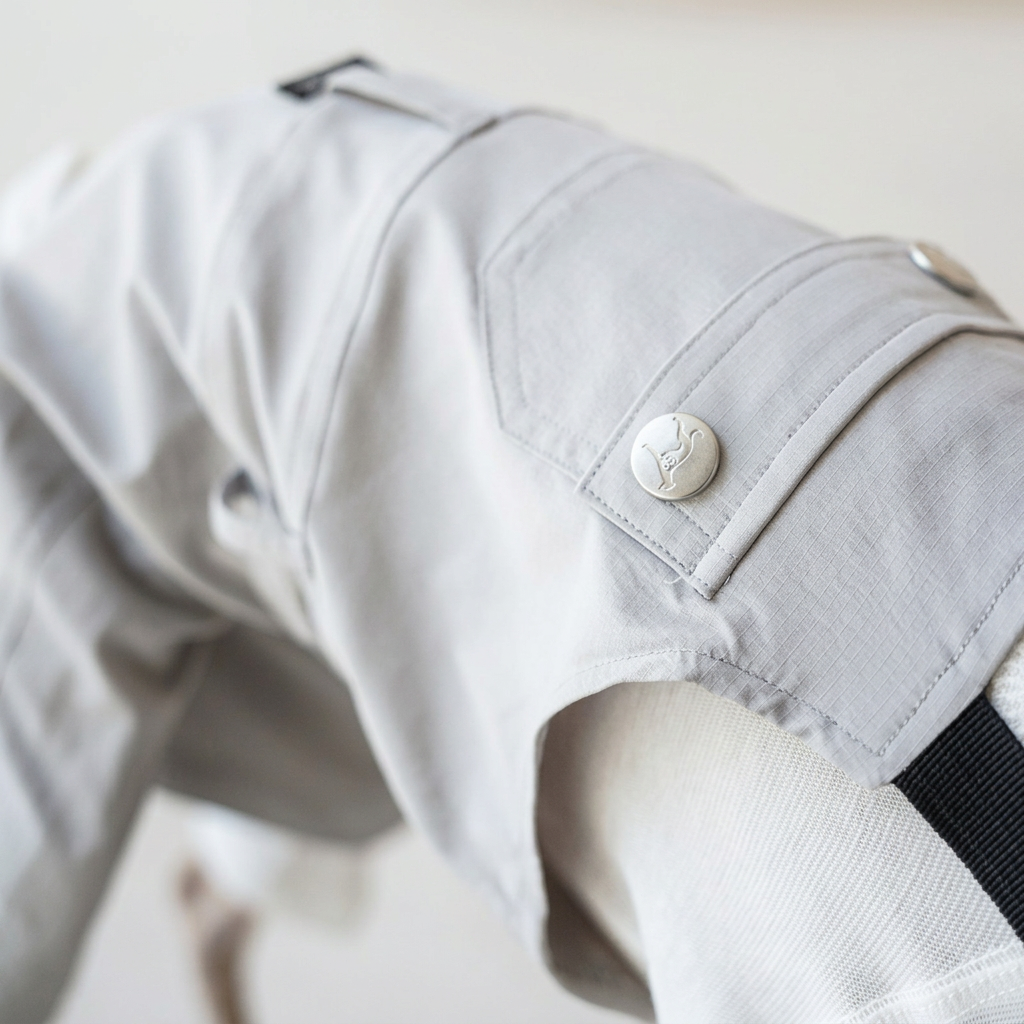 Close-up of White Urban Explorer overalls showing the engraved round button, panelled seams, fabric texture and black strap.