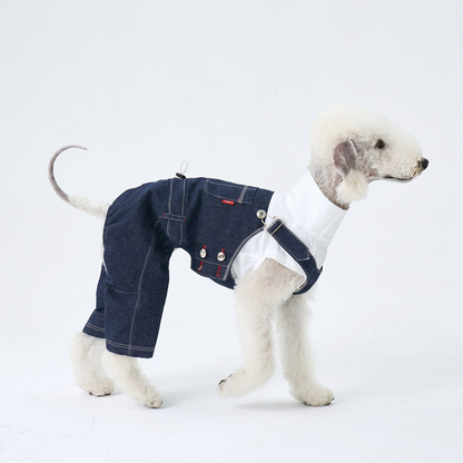 Side view of a white dog wearing dark indigo denim overalls with silver buttons, white stitching and rear-leg coverage over a separate white top.