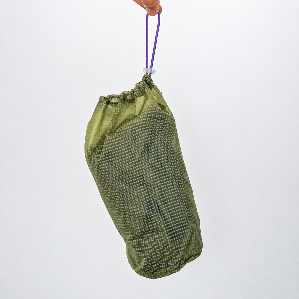 Mist Green LightShield storage pouch with grid-textured nylon, purple drawstring and grey cord lock, held by its drawstring.